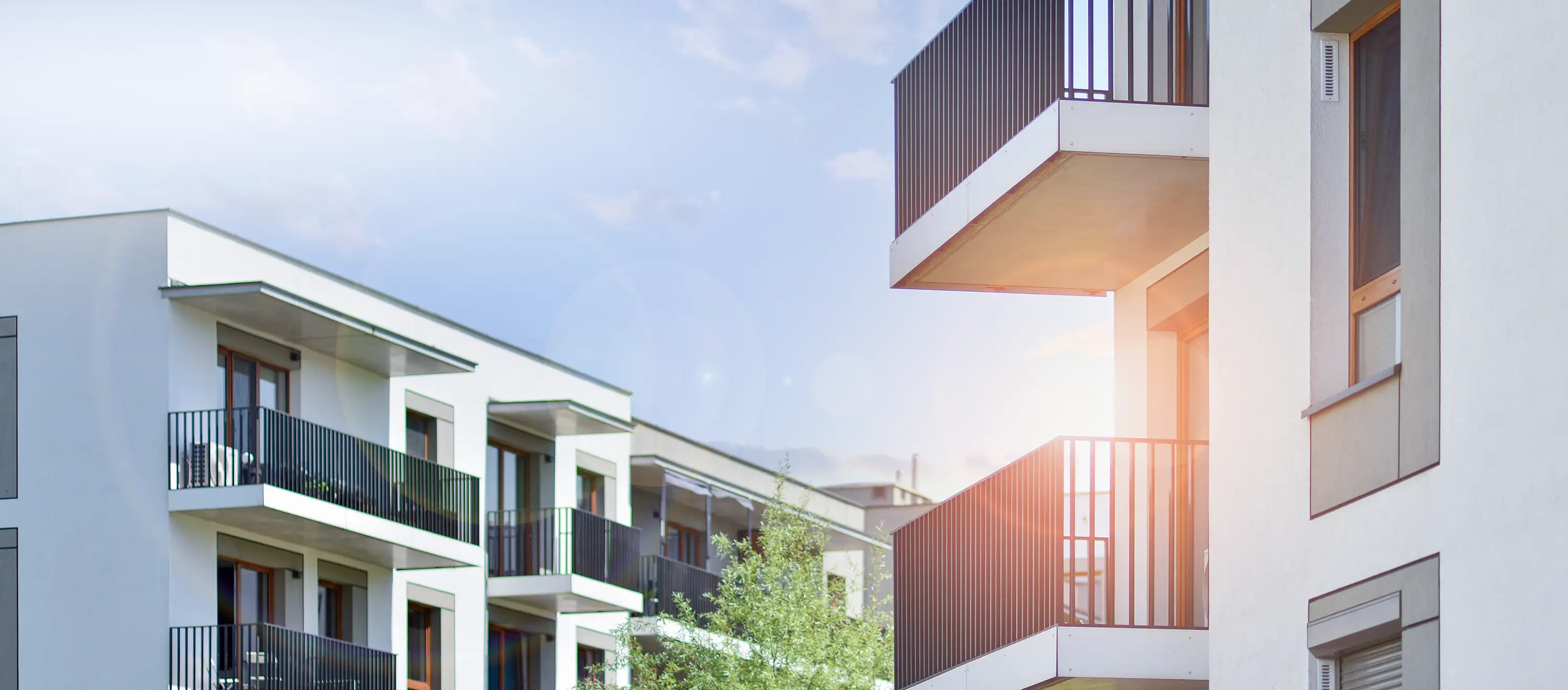 Seher Startbild Unternehmen: modernes Wohnquartier mit Balkonen, Bäumen und Himmel